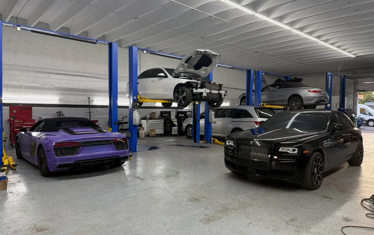 Two of the shop's lifts in use, a car raised with its front end stripped, a Rolls-Royce and a purple Audi R8 on the floor beside them.