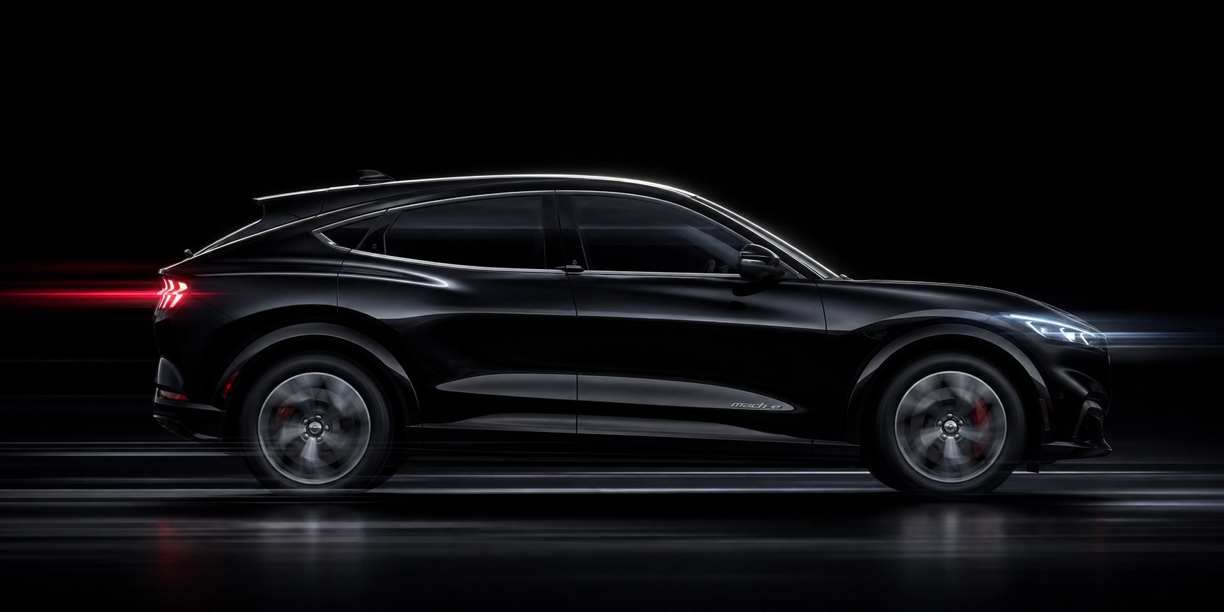 A black Ford Mustang Mach-E in full profile against a dark studio backdrop, nose to tailgate, the length of the body a calibration has to be measured against
