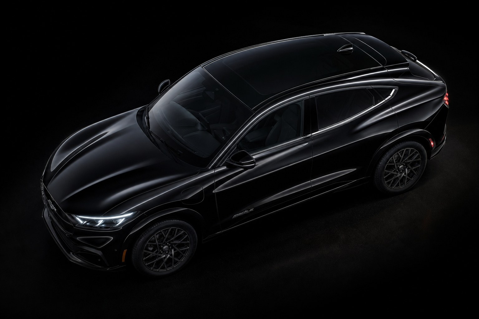A black Ford Mustang Mach-E on a dark studio floor, seen three-quarter from above the front wing