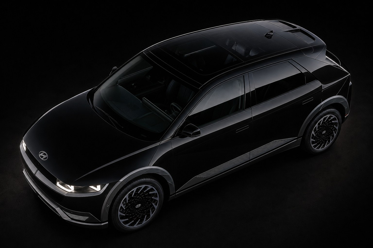 A black Hyundai Ioniq 5 against a dark studio background, seen from above and ahead of the front wing: roof, bonnet, the full length of the flank and the aero wheels — the panels a collision repair works on