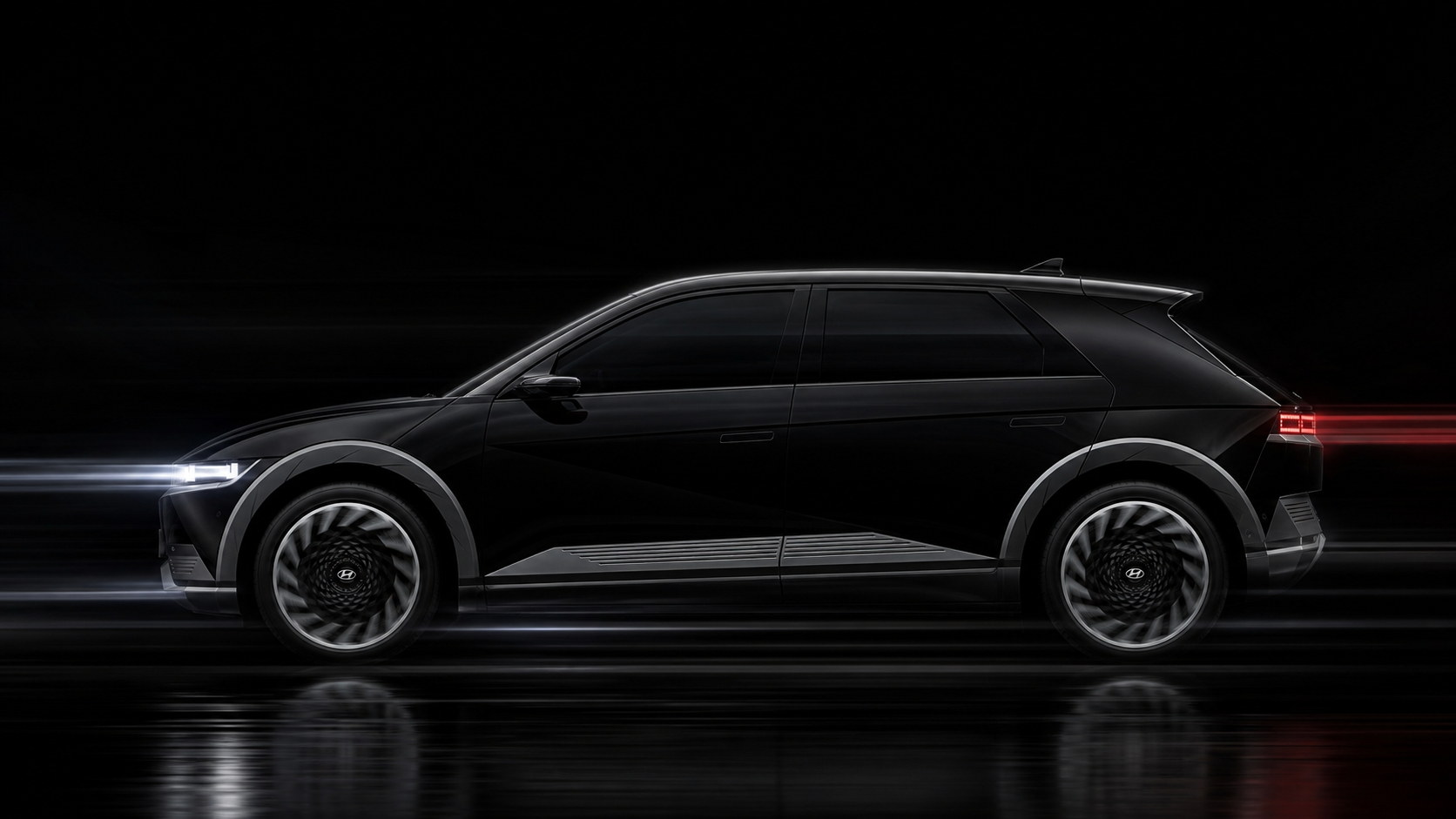 A black Hyundai Ioniq 5 in full profile against a dark studio backdrop, light streaking past it at headlamp and tail-lamp height — the length of the body a calibration has to be measured against