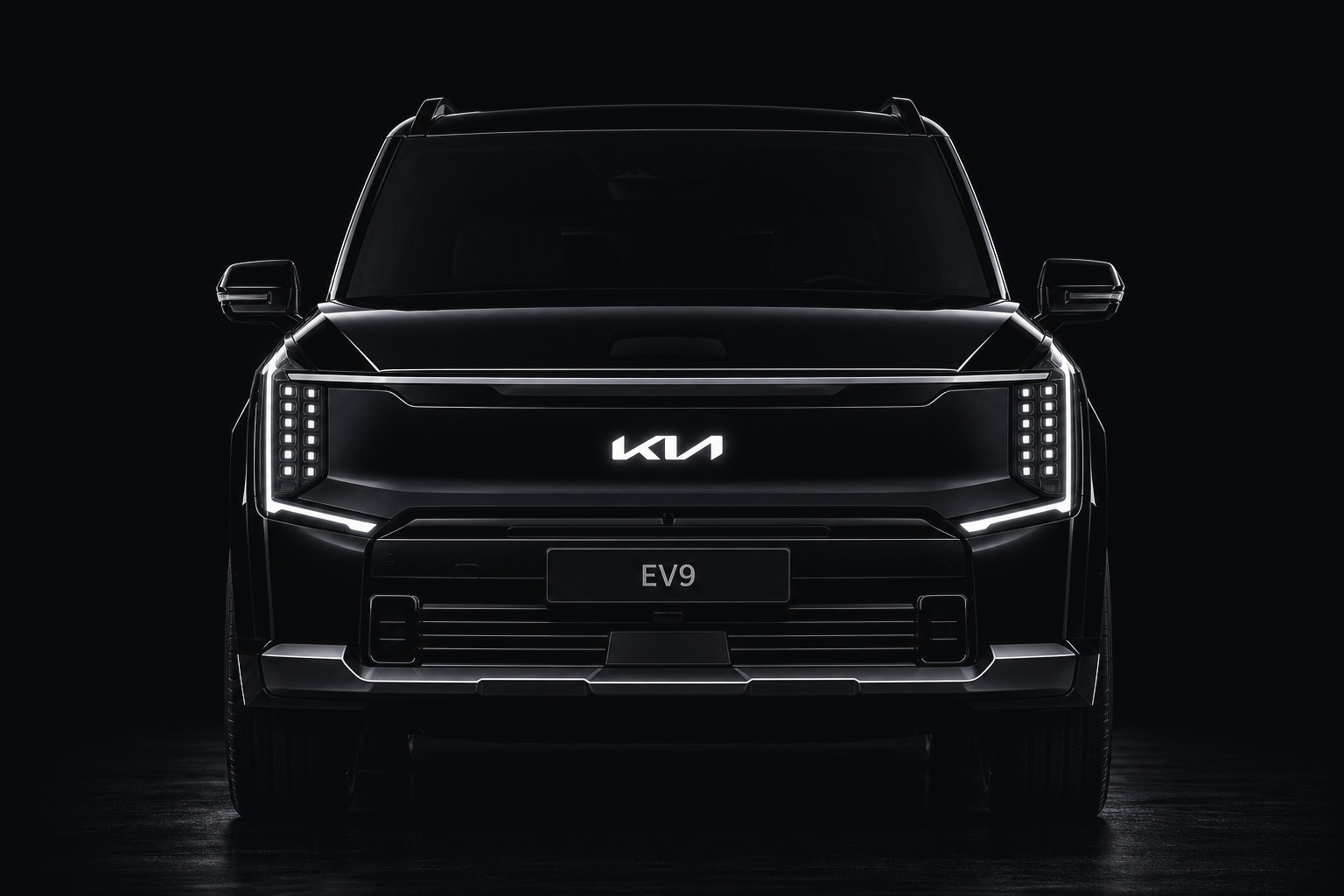 The front of a black Kia EV9 seen head-on against a dark studio ground: the full-width light bar, the grille panel, the lower bumper and both front wheels — the panels a collision repair replaces