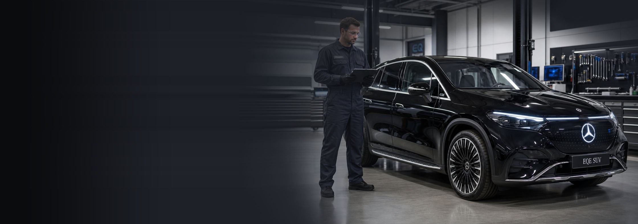 A black Mercedes-Benz EQE SUV standing three-quarter front on inside a workshop bay, a technician with a tablet beside it