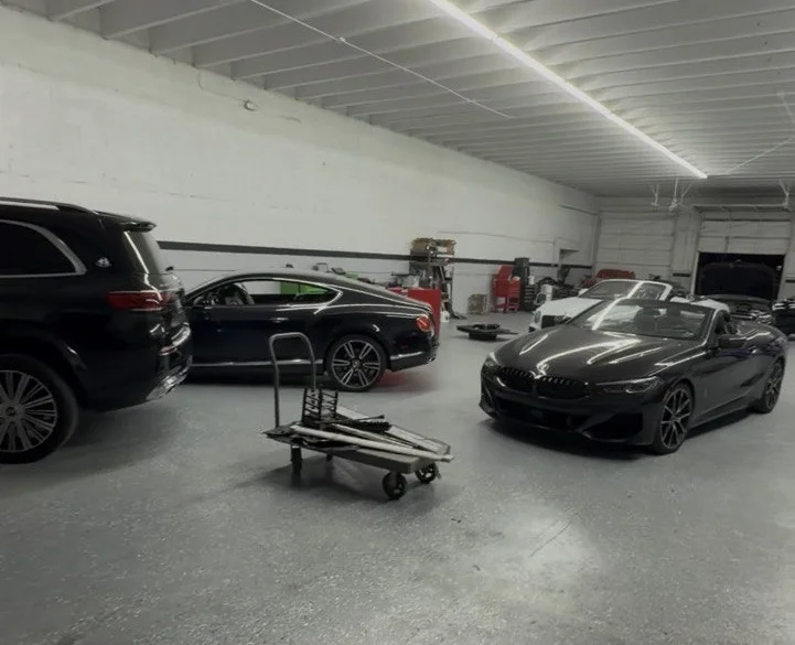 A dark BMW 8 Series convertible parked inside the shop, with a Bentley coupe and an SUV standing behind it.