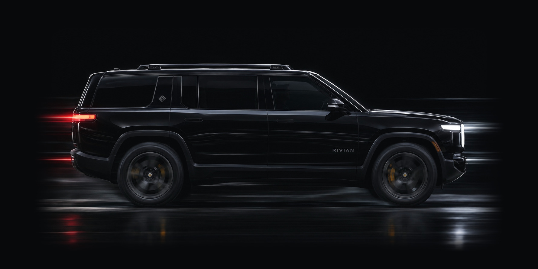 A black Rivian R1S in full profile against a dark studio ground, the length of the body a calibration has to be measured against